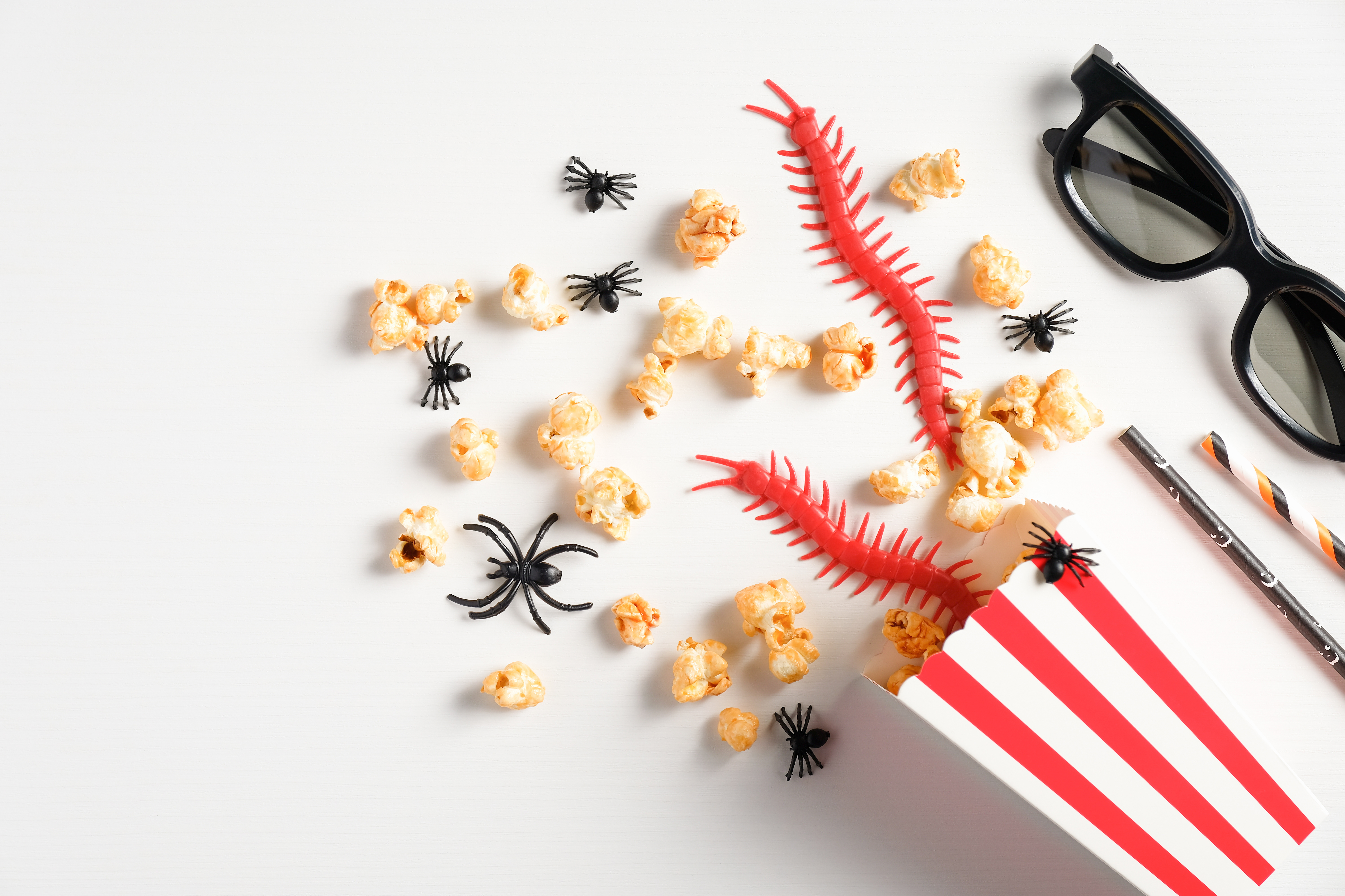 Halloween party background. Flat lay composition with popcorn, halloween decorations, 3d glasses on white table. Watching halloween horror movie at night concept.